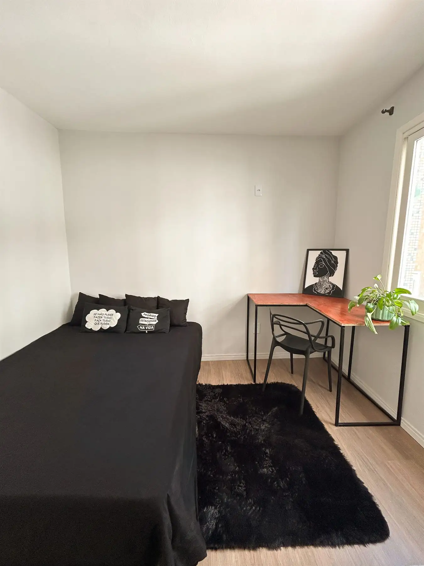 Estúdio com cama de casal, tapete e mesa de trabalho junto à janela